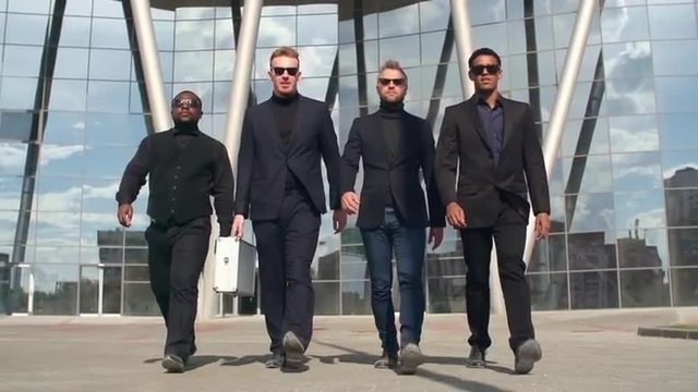 Criminal gang in suits and sunglasses walking towards the camera with aluminum briefcase