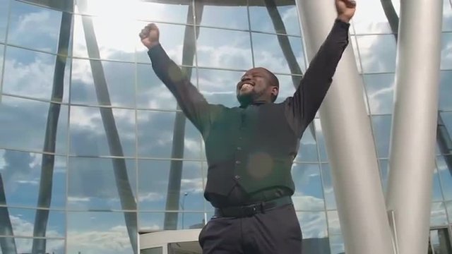 African man full of happiness yelling and raising his arms in front of office center 