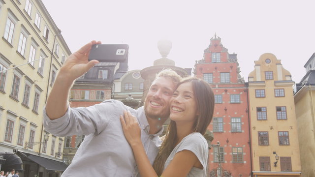 Couple taking self portrait selfie photo on Europe travel. Happy candid tourists on Stortorget, big square, Gamla Stan, the old town of Stockholm, Sweden. Asian woman, Caucasian man.