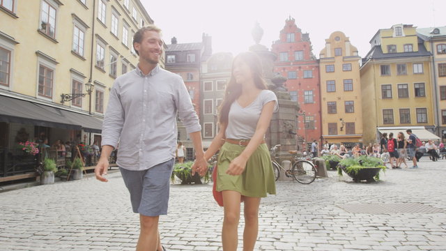 Couple walking holding hands in city of Stockholm, Sweden, Europe. Happy multiracial young couple walking outside on Stortorget big square in Gamla Stan, the old town. Scandinavian man, Asian woman.