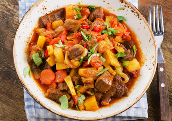 Beef stew with vegetables on a rustic wooden table.