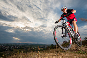 Mountain biker with helmet jumping against blue evening sky. Low angle portrait. Extrem sport donwhill cyclist