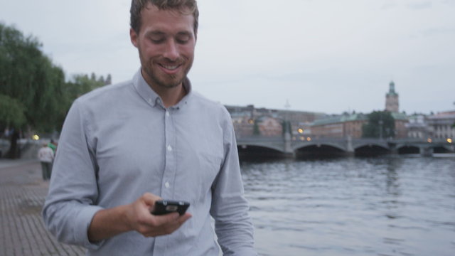 Man smart phone sms texting using app at night in city of Stockholm. Handsome young business man using smartphone smiling happy wearing shirt outdoors. Urban male professional in his 20s.