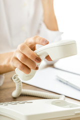Female hand picking or hanging up white telephone receiver