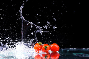 Fototapeta na wymiar Studio shot with freeze motion of cherry tomatoes in water splash on black background with copy space