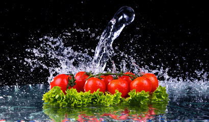 Panele Szklane  Świeże pomidory wiśniowe i zielona świeża sałatka z kroplą wody na ciemnym tle Makro krople wody spadają na czerwone pomidory czereśniowe i robią plusk