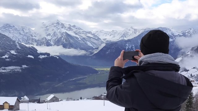 A young boy is taking a magnificent picture of frosty Alps with his phone
