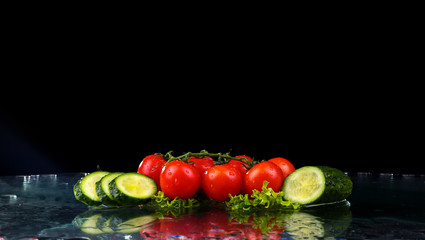 Studio shot with freeze motion of cherry tomatoes and slices of cucumber in water splash on black background