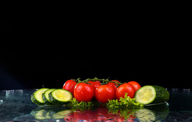 Studio shot with freeze motion of cherry tomatoes and slices of cucumber in water splash on black background