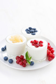 Natural yogurt with fresh berries in glass jars on white table