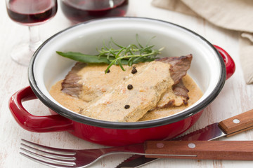 fried pork with pepper sauce in dish and red wine on white wooden background