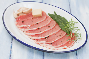 raw pork on dish with bay leaf, black pepper and garlic