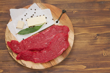 raw beef with butter, herbs and black pepper on wooden board on brown wooden background