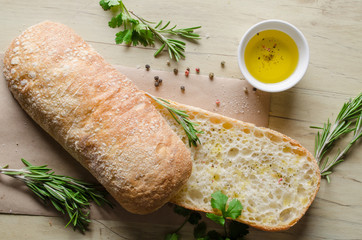 Sliced bread ciabatta watered with extra virgin olive oil with herbs  on wooden background. View from above.