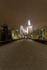 Night snowy Prague Bridge Tower and St. Nicholas' Cathedral from Charles Bridge with its Statues, Czech republic