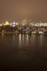 Fototapeta na wymiar Night romantic snowy Prague gothic Castle with Charles Bridge and St. Nicholas' Cathedral , Czech republic
