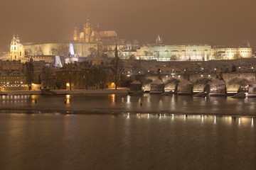 Fototapeta na wymiar Night romantic snowy Prague gothic Castle with Charles Bridge and St. Nicholas' Cathedral , Czech republic
