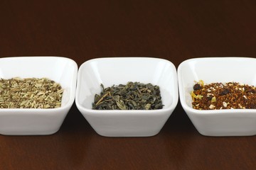 Three sorts of tea leaves in square plates on brown wooden table, positioned horizontally