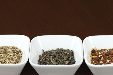 Three sorts of tea leaves in square plates on brown wooden table, positioned horizontally with space for text above