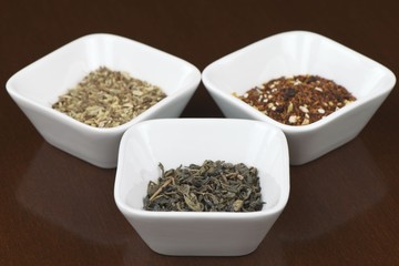 Three sorts of dry tea leaves in square plates on brown wooden table with reflection