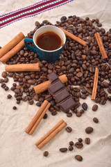 Cup of hot coffee with cinnamon sticks, bitten bar of chocolate