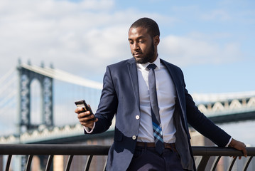 Young businessman using mobile phone phone with Manhattan Bridge in the background.