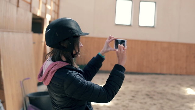 Young, woman with helmet taking photo at a stable

