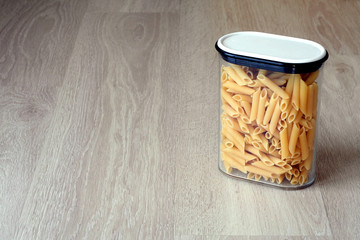 Uncooked pasta in a transparent jar, wooden background, with copy space