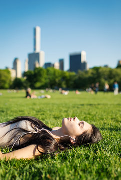 Young Woman Relaxing In Central Park Laying On The Grass And Listening To Music. New York.