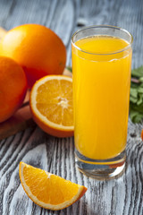 Glass of fresh orange juice, mint leaves and orange slices on wooden table