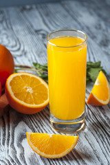 Glass of fresh orange juice, slices of orange and mint leaves on wooden table. Focus on orange slice.