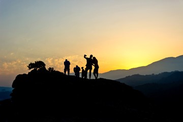 Silhouettes of people resting on top of rock and looking at golden sunset