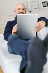 älterer mann entspannt zuhause und liest am tablet