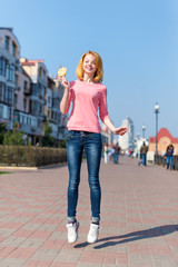 Obraz premium Redhead beautiful young woman jumping high in air over blue sky holding colorful lollipop. Pretty girl having fun outdoors.