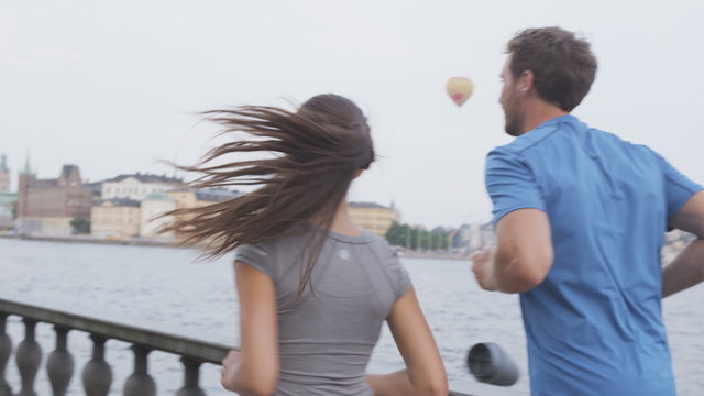 Runners people. Healthy couple running in Stockholm city cityscape background. Riddarholmskyrkan church in the background, Sweden, Europe. Healthy multiracial young adults, asian woman, caucasian man.