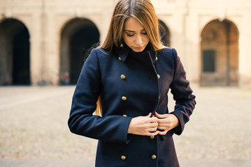 Young woman closing coat outdoors. Parma, Italy.