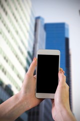 Hand holding smartphone against low angle view of skyscrapers