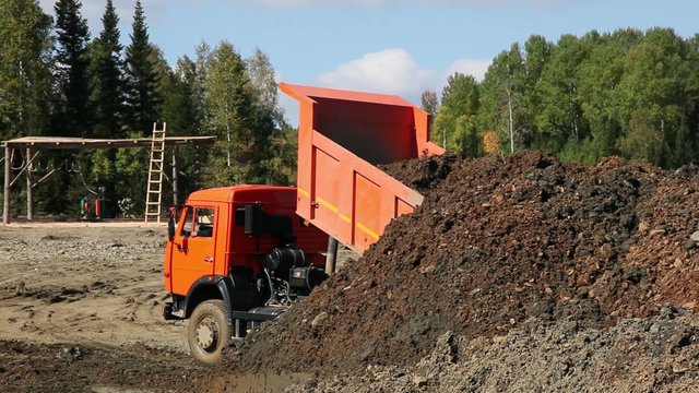 A dump truck unloads the ground. gold mining in Siberia.Pours ore truck, bulldozer shovel it. The red truck. Tractor. 