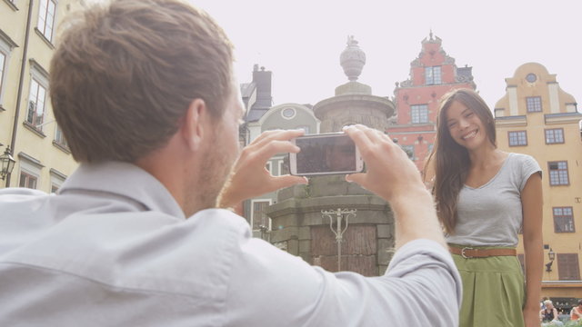 Boyfriend taking picture of girlfriend using smart phone. Couple in love dating having fun using smartphone taking photos. Tourists visiting Stockholm, Sweden. Multiracial Asian woman, Caucasian man.