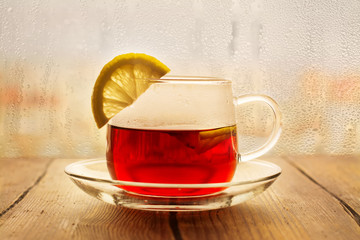 Black tea with lemon slices in a glass cup. View over wet rainy window. Toned image. Selective focus