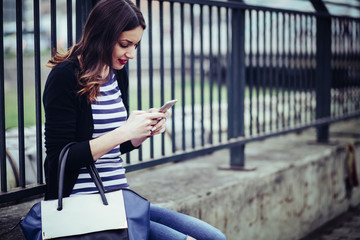 beautiful young woman looking at smart phone in city/ young smiling woman looking at her smartphone