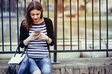 beautiful young woman looking at smart phone in city/ young smiling woman looking at her smartphone