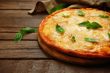 Tasty pizza decorated with basil and cotton napkin on wooden background