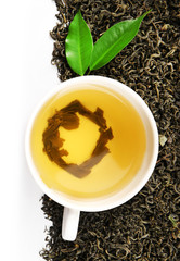 Cup with brewed dry tea and green leaves, isolated on white