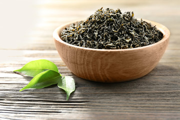 Dry tea with green leaves in bowl on wooden table background