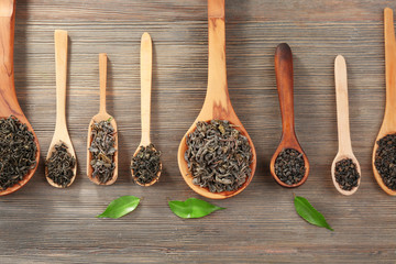 Dry tea with green leaves in wooden spoons on table background