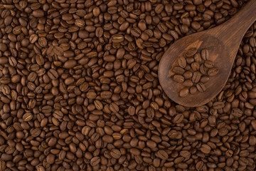 Wooden spoon on roasted coffee beans, background.