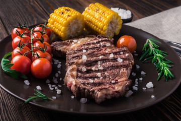 Grilled beef steak ribeye with cherry tomatoes, rosemary and corn on wooden background