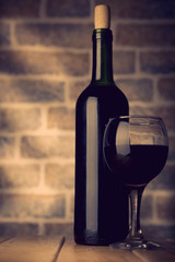 Wine bottle and glass on a wooden table with bricks wall backgro