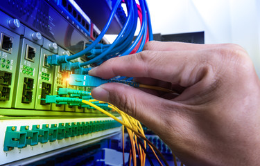 Man connecting fiber network cables to switches